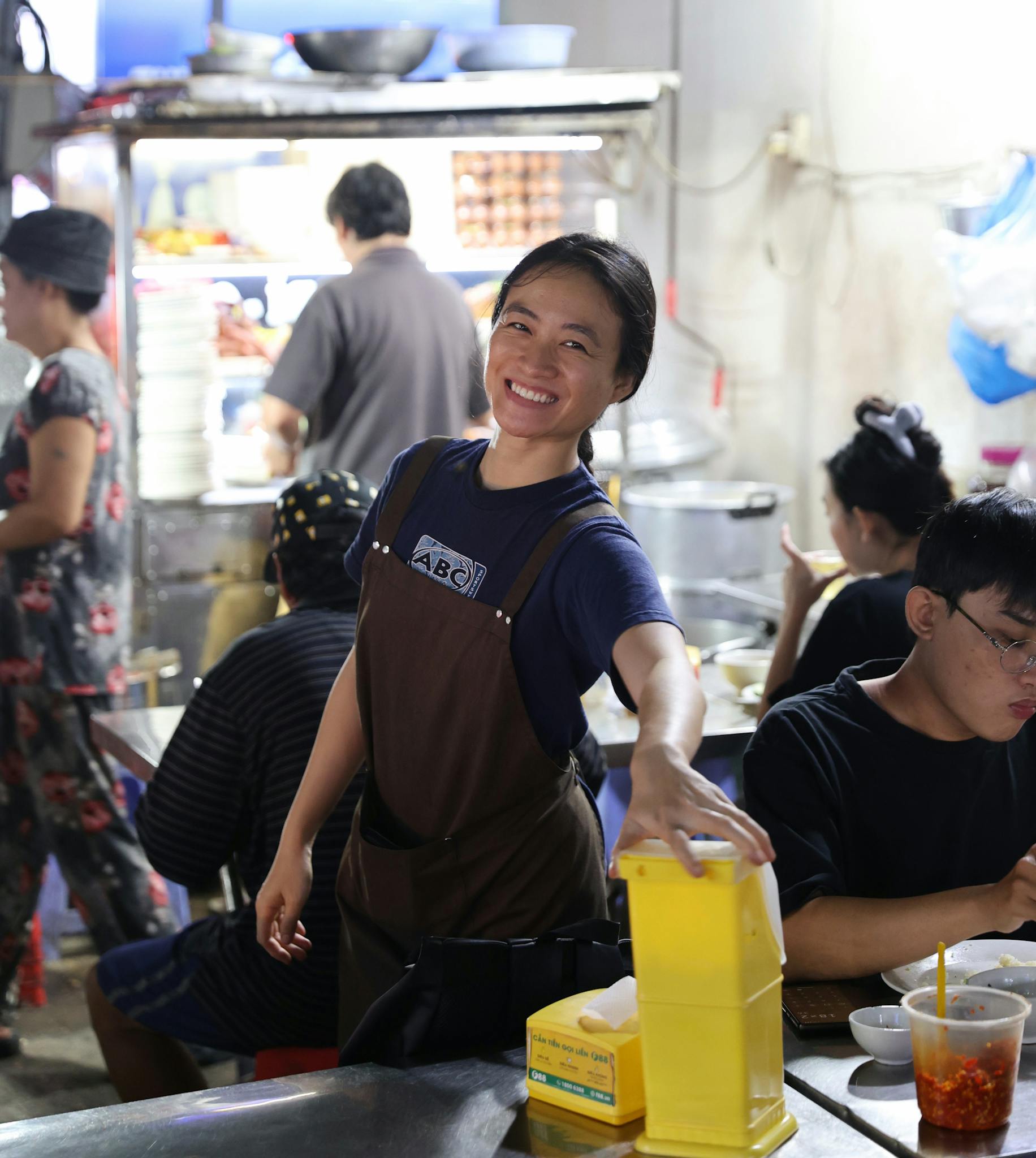 A cheerful chef working at a bustling Asian street food stall indoors.