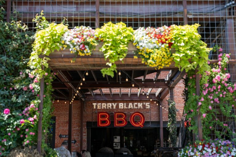 Entrance of Terry Black's BBQ with vibrant flowers in Dallas, Texas.