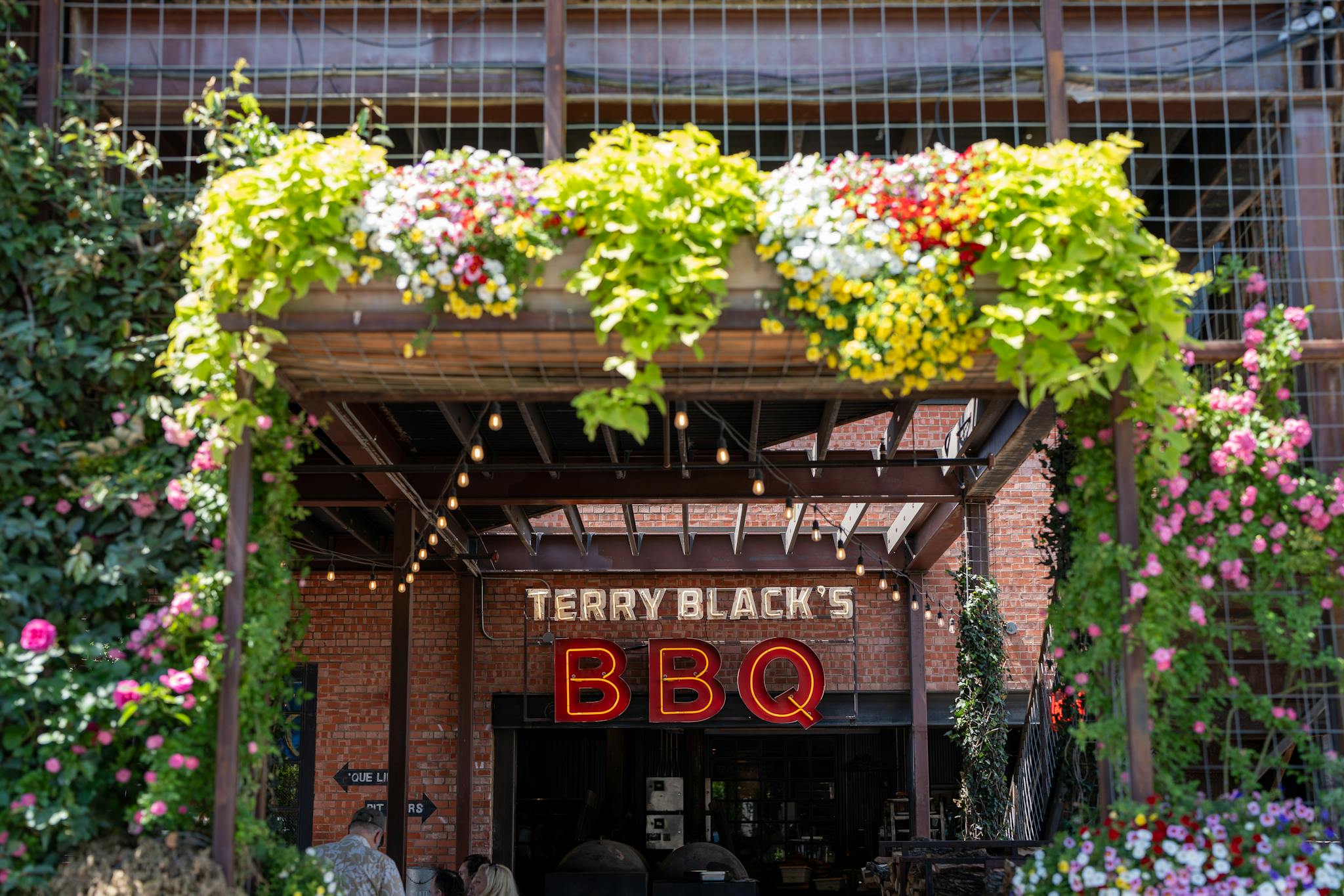 Entrance of Terry Black's BBQ with vibrant flowers in Dallas, Texas.