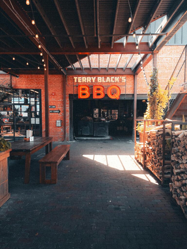 Terry Black's BBQ entrance in Dallas, TX with rustic outdoor seating and firewood.